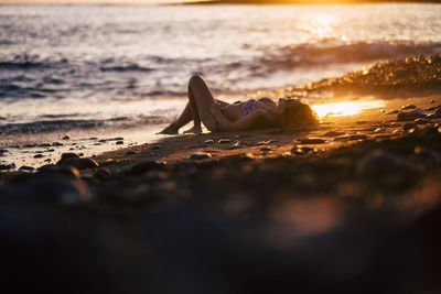 Woman lying on sand at beach during sunset