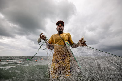 Man fishing in water against cloudy sky