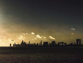 Silhouette buildings by sea against sky during sunset