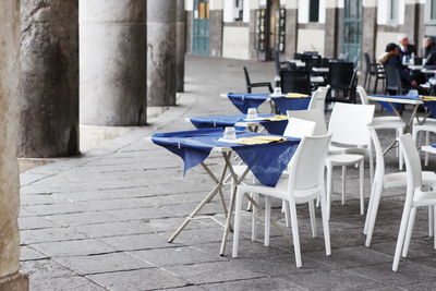 Empty chairs and tables at sidewalk cafe amidst buildings