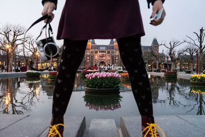 Low section of woman with reflection in canal against sky in city