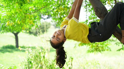 Cute little girl playfully hangs from a tree limb. summer time, heat, childhood. funny portrait