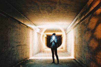 Young woman with flashlight standing against wire wool in tunnel