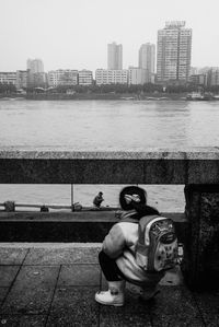 Man sitting by river against buildings in city