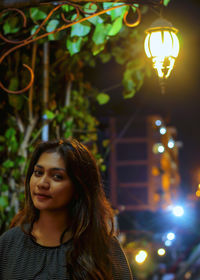 Portrait of young woman against illuminated lamp post