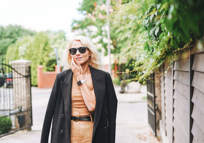 Adult elegant blonde woman in black jacket and sunglasses on summer city street