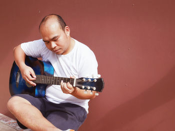 Man playing guitar against wall