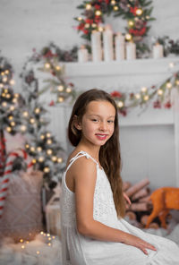 Portrait of smiling young woman sitting on christmas tree