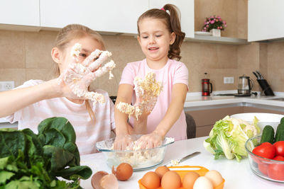 Sisters kneading dough in kitchen at home