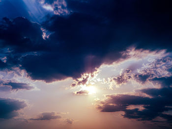 Low angle view of sunlight streaming through clouds