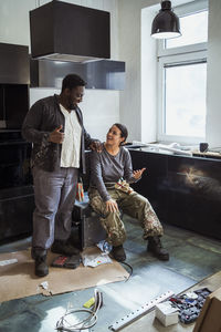 Cheerful multiracial male and female carpenters discussing together in kitchen of apartment