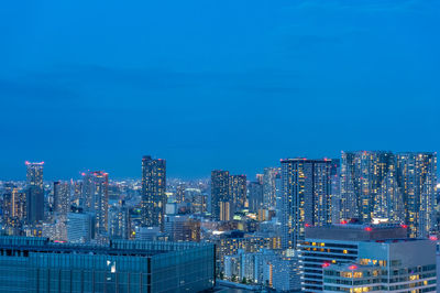 Illuminated buildings in city against blue sky