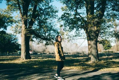 Full length portrait of young woman standing against trees