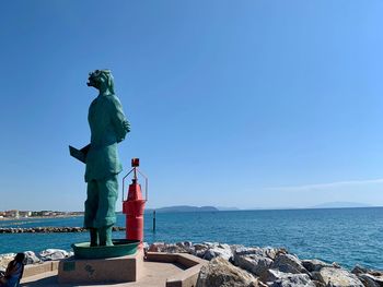 Statue by sea against clear blue sky