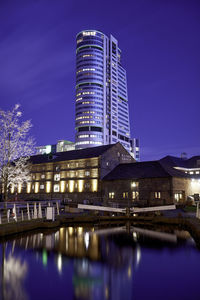 Illuminated buildings by river against sky at night