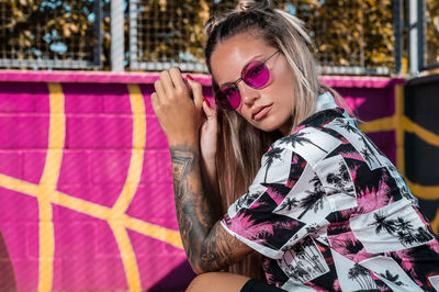 Attractive woman in trendy summer clothes sunglasses and a tattooed arm on a pink sports track