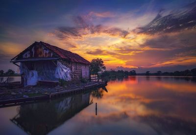 House by lake against sky during sunset