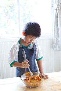 Boy preparing food in bowl on table at kitchen