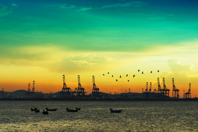 Silhouette cranes against sky during sunset