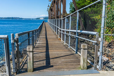 Wooden walkway leading towards sea against sky