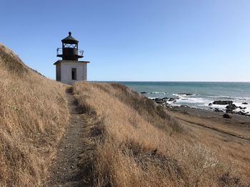 Lighthouse by sea against clear sky