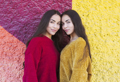 Smiling sisters standing by multi colored wall