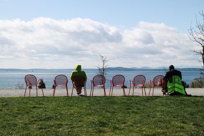 Rear view of people sitting at beach on sunny day