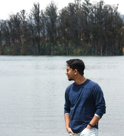Young man looking at lake against trees