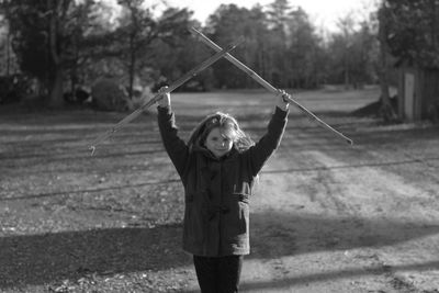 Portrait of girl holding sticks while standing at field