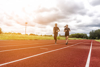 People running on sports track against cloudy sky