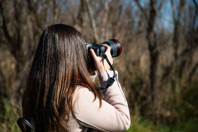 Beautiful woman taking a picture of a dry trees forest back shot closeup person