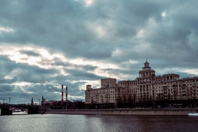 Buildings by river against cloudy sky