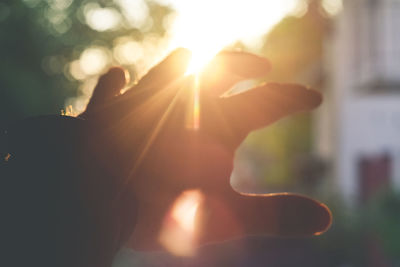 Close-up of hands against sun during sunset