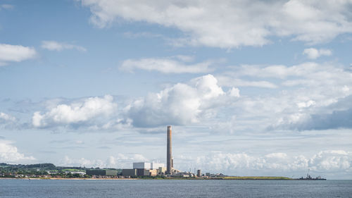 Panoramic view of factory by sea against sky