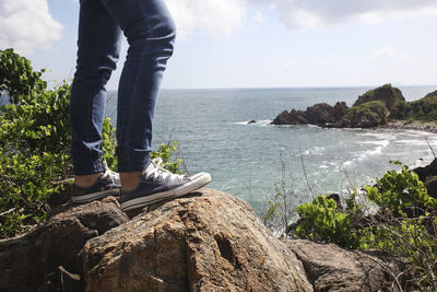 Low section of person on rock by sea against sky
