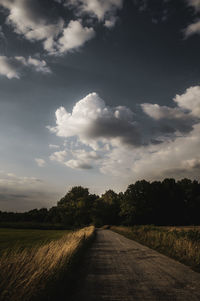 Empty road amidst field against sky