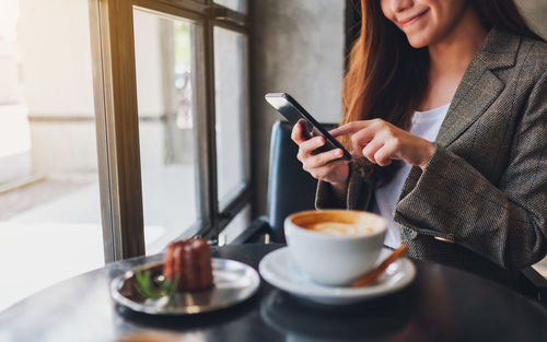 Midsection of businesswoman using mobile phone while having coffee at restaurant