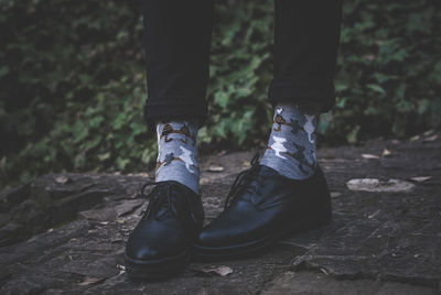 Low section of man wearing black leather shoes while standing in forest