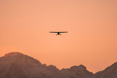 Low angle view of silhouette airplane against orange sky