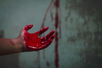 Cropped hand of person with blood against wall