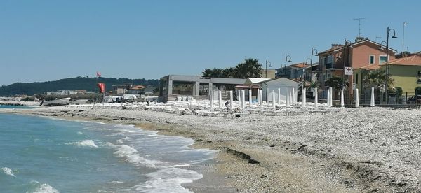 Houses on beach by buildings against clear blue sky