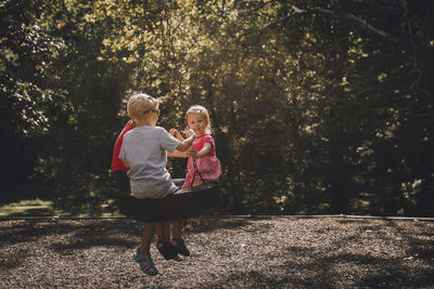 Siblings sitting on swing at park