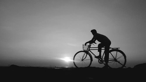 Silhouette man with bicycle against sky during sunset