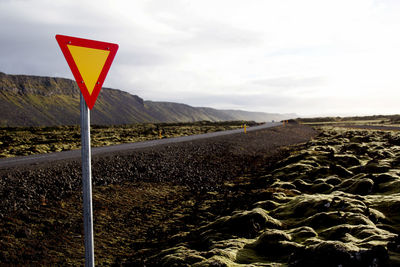 Road sign on field against sky