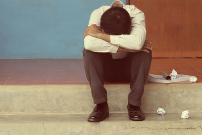 Depressed man hugging knees while sitting on tiled floor