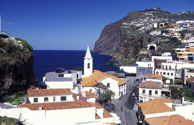 Bell tower in town by sea against clear blue sky