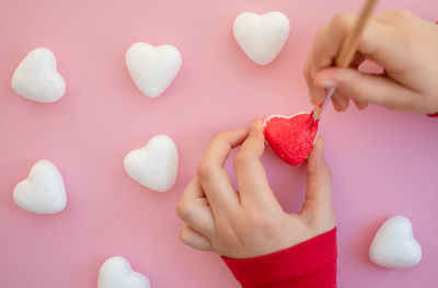 Cropped hand of woman holding heart shape against wall