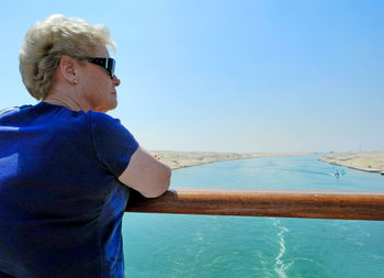 Rear view of senior woman standing by railing against blue sky