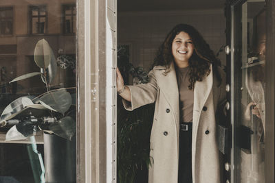 Portrait of smiling businesswoman wearing overcoat while standing near door at office