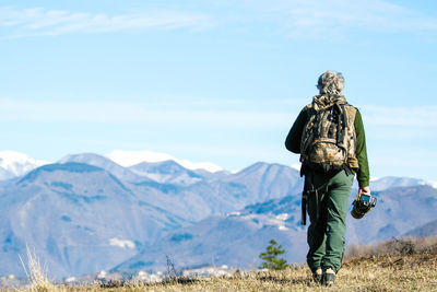 Rear view of man walking on snowcapped mountain against sky